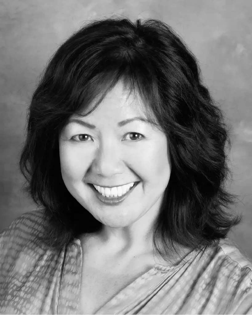 Black-and-white head-and-shoulders portrait of a smiling Asian woman with shoulder-length dark hair and a patterned blouse.